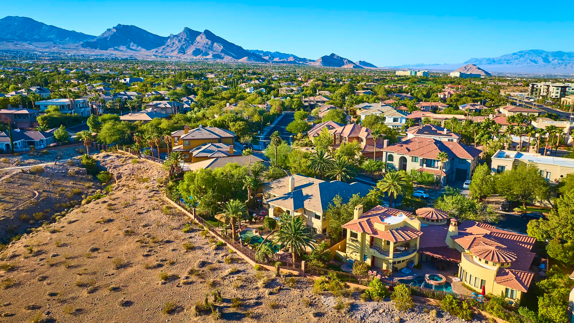 Hillside neighborhood of large tile-roofed homes with open desert in the foreground
