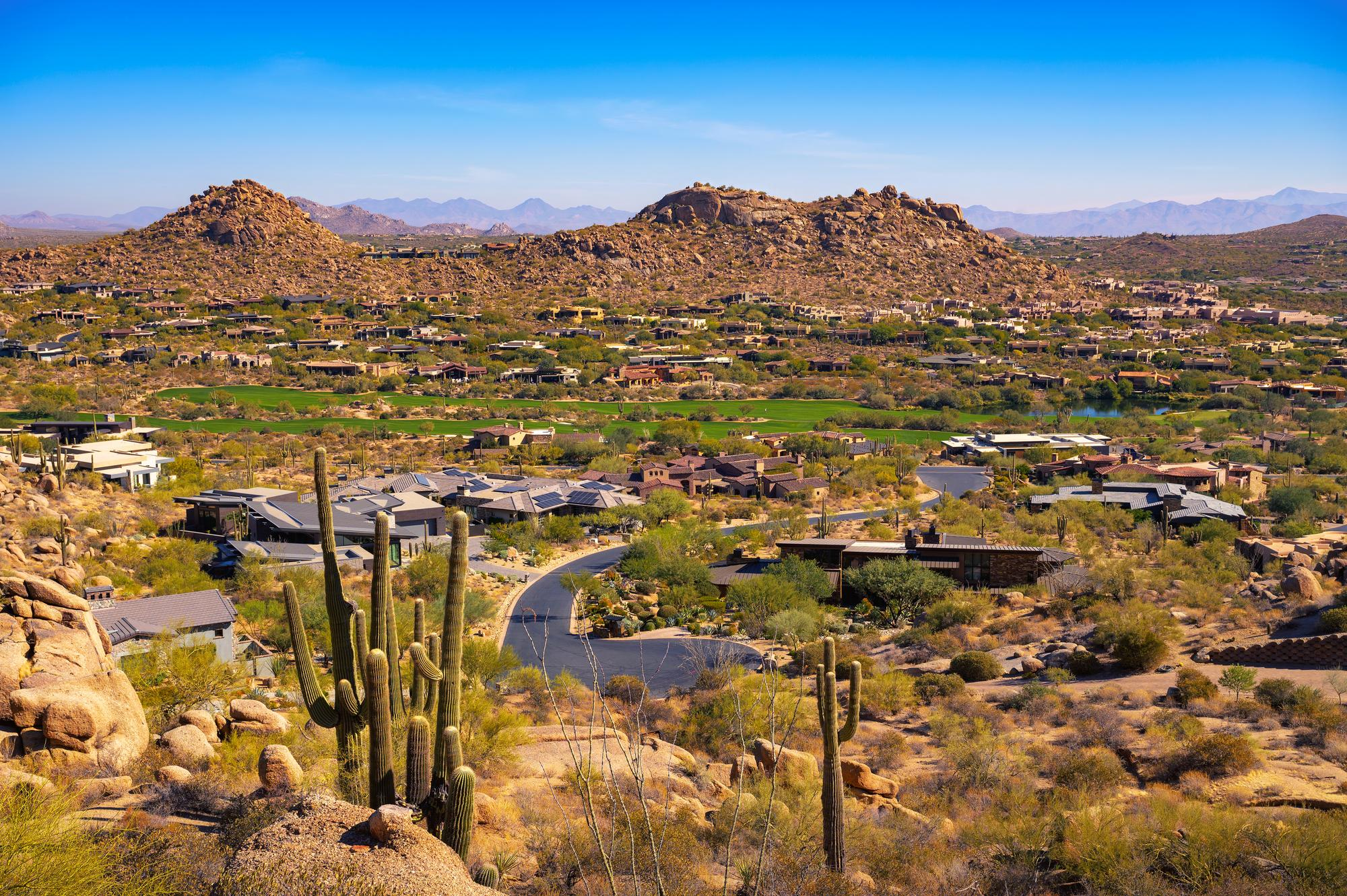 Desert homes among saguaros and granite boulders with mountains beyond