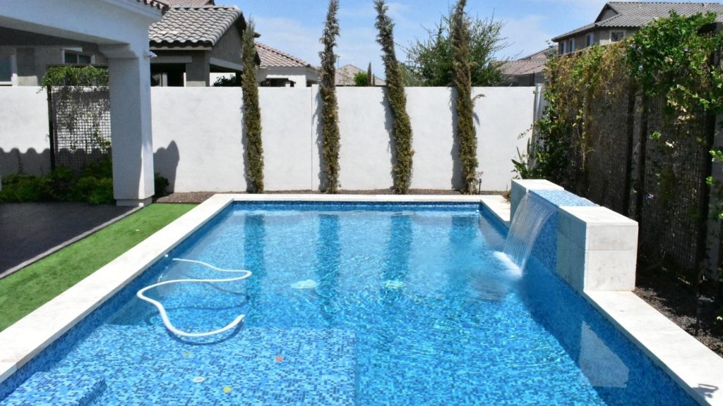 Backyard swimming pool with a water feature beside a modern home