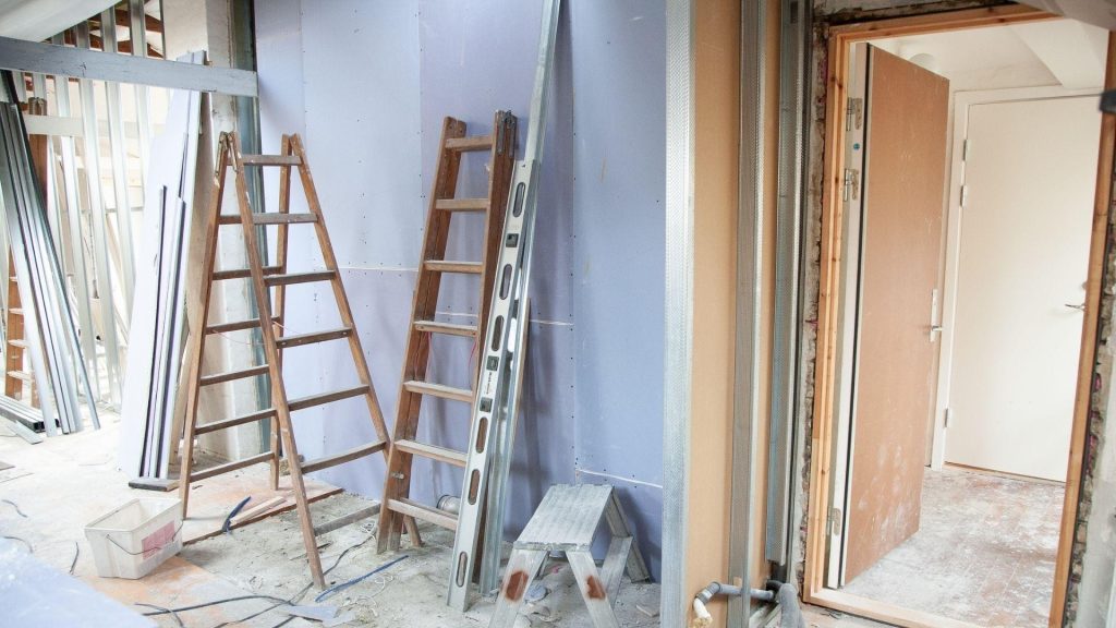 Interior renovation in progress with ladders, paint supplies and bare walls